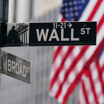 The image shows the iconic "WALL ST" street sign at its intersection with "BROAD ST" in New York City's financial district, with an American flag blurred in the background. The image visually anchors the post's commentary, as the Wall Street sign directly represents the financial institutions and banks that the Etherealize CEO criticizes for pursuing closed, permissioned blockchain strategies rather than open, public networks.