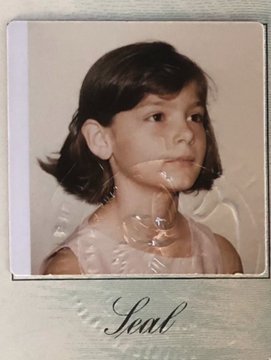 A vintage photograph of a young girl with dark hair wearing a frilly dress is shown in a polaroid-style frame with the word "Seal" written in cursive at the bottom. The image likely depicts a child in Communist-era Eastern Europe, evoking the personal gratitude expressed in the caption celebrating America's role in saving the poster's family from communism.