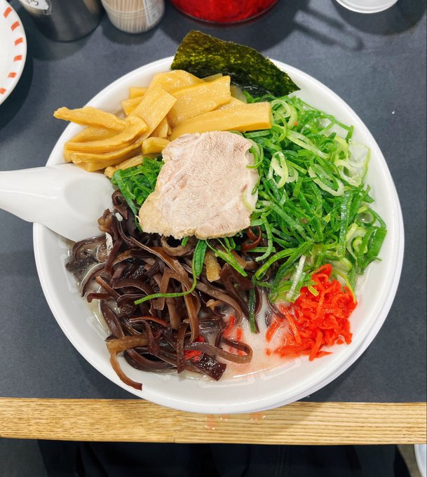 A bowl of ramen topped with chashu pork, bamboo shoots, nori seaweed, green onions, wood ear mushrooms, and red chili.