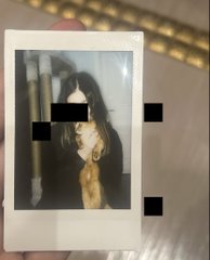 A hand holds an instant Polaroid-style photo of a person with long hair, with portions of the image censored by black rectangles.