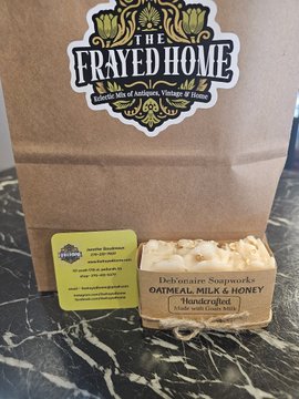 A bar of "The Frayed Home" handmade "Oatmeal Milk & Honey" soap sits in front of its branded brown paper packaging and a yellow Square merchant card on a marble countertop, illustrating a local Kentucky business accepting Bitcoin through a Square terminal.