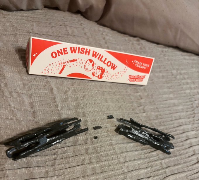 An open pack of 'One Wish Willow' snack crackers revealing dark black licorice-like candy pieces scattered on a gray fabric surface, with the packaging noting it 'Amazes your friends' since you only get one wish.