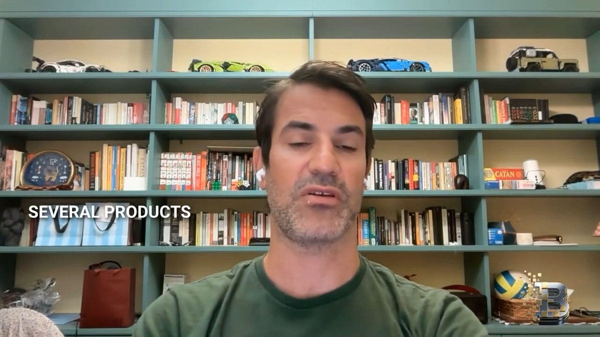 A man in a green t-shirt speaking in front of a bookshelf filled with books, model cars, and a Catan board game, with the subtitle 'SEVERAL PRODUCTS' visible.