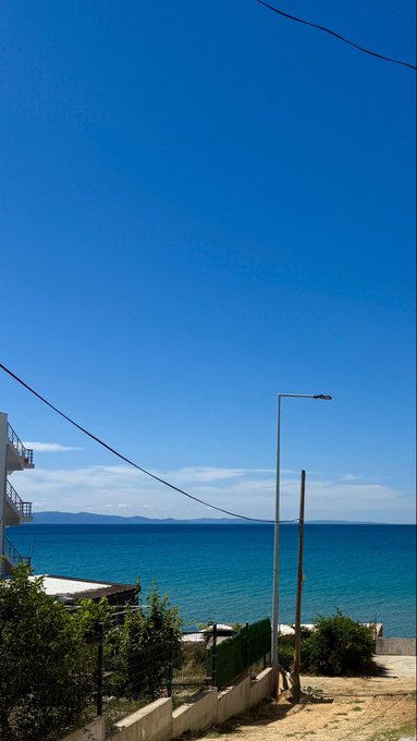A clear, sunny morning view of a calm blue sea with distant mountains, a streetlamp, and power lines framing the scene, perfectly capturing the peaceful start to a day as greeted with "Goodmorning legends!"
