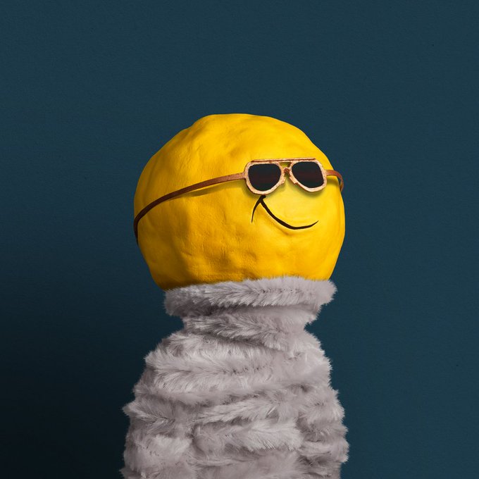 A yellow smiley face drawn on a round object wearing orange-tinted sunglasses, set against a dark teal background with a fluffy gray collar visible below.