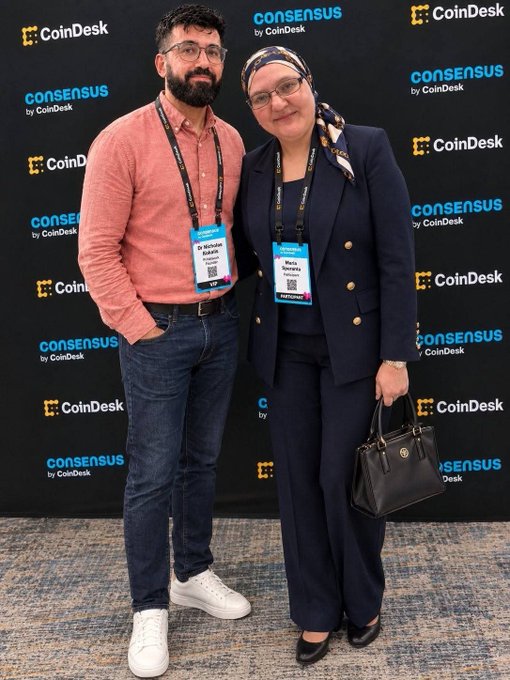 Two attendees pose in front of a "CoinDesk Consensus" step-and-repeat backdrop, with the woman wearing a name badge that reads "Dr. Maria Stankevich" (Chief Business Development Officer) and the man sporting a "consensus" lanyard. The image relates to the post as it captures the moment the Pi Network pioneer met Dr. Nicholas Kokkalis at the prominent Consensus conference.