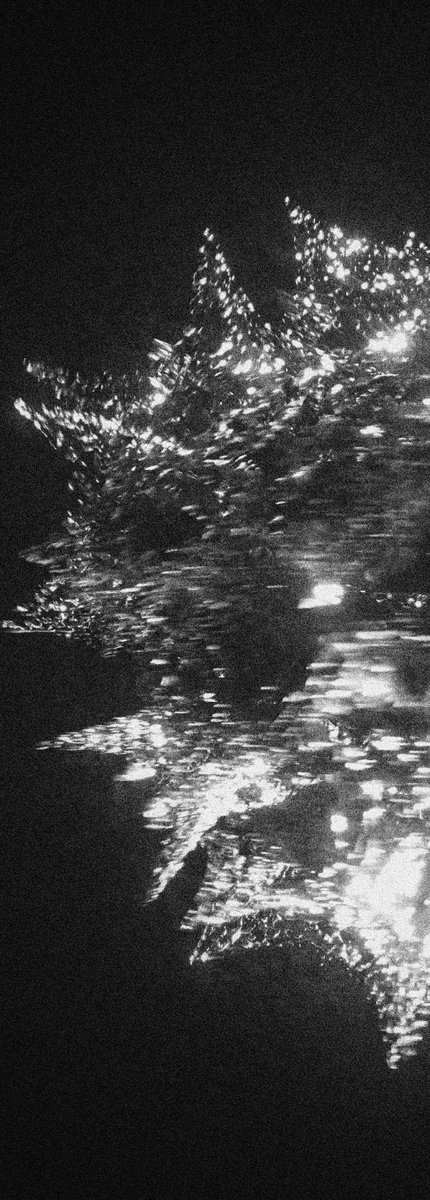 A black and white photograph captures the shimmering reflections of light on water at night.