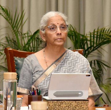 Finance Minister Nirmala Sitharaman is shown seated at a desk with a tablet, appearing focused during a discussion, as the post highlights her address on AI and quantum threats to cybersecurity in the financial sector.