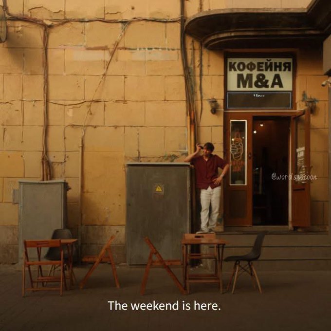 A man standing in front of a coffee shop called "КОФЕЙНЯ M&A" in Russian, with text at the bottom reading "The weekend is here."