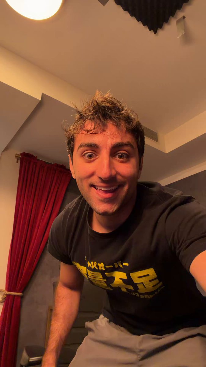 The image features a man wearing a black t-shirt with yellow text that reads "I have 8,000$ in hype". The man appears to be smiling for the camera while posing in front of a red curtain. The caption below the photo suggests that the person is promoting or discussing this particular brand or product.
