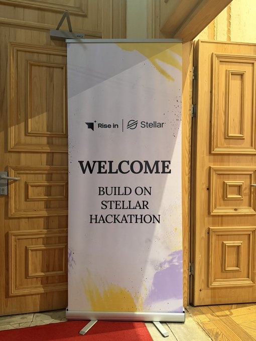 A welcome banner at the Rise in x Stellar "Build on Stellar Hackathon" stands between ornate wooden doors on a red carpet, marking the entrance to the Istanbul Pro Hackathon event.