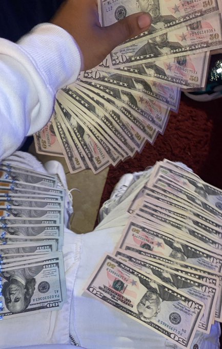 A person displays a fan of US $50 bills while sitting on a bed with several more bills spread out on the white bedding.