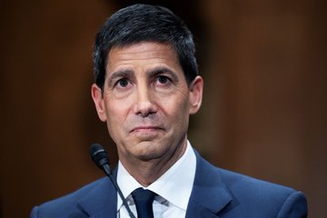 A man in a dark suit and tie sits before a microphone with a serious expression, likely during a formal hearing or testimony. His solemn demeanor suggests he may be a financial official or regulator, fitting the post's theme of Federal Reserve monetary policy and its impact on crypto markets.