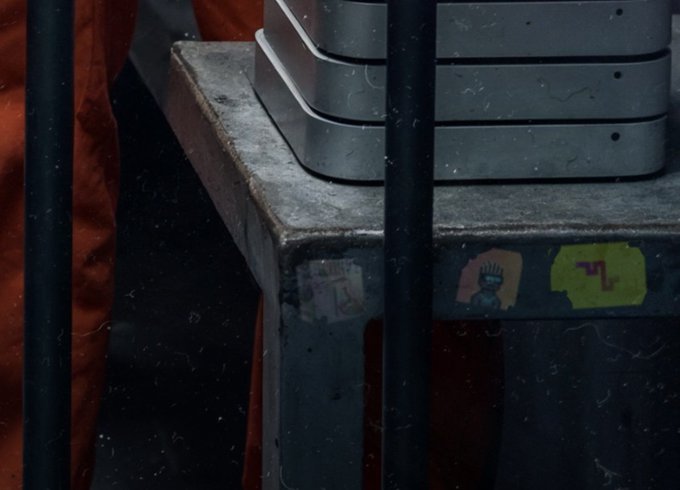 A close-up of a dusty, industrial-looking metal surface with a couple of worn stickers, including one with a symbol, and metal bars in the foreground.