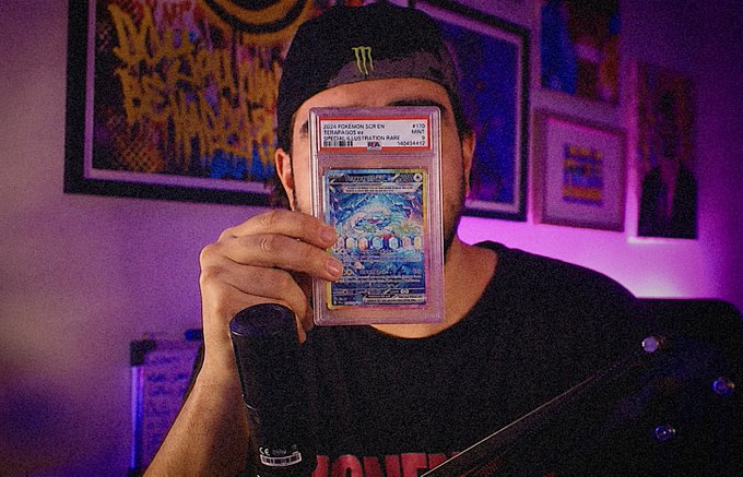 A person wearing a Monster Energy cap holds up a graded PSA 10 Pokemon card in front of their face, with purple lighting and a framed poster in the background.