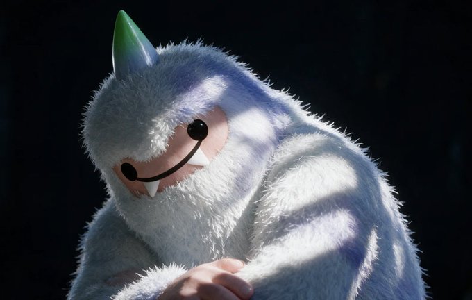 A person in a fluffy white Yeti mascot costume with a rainbow-colored horn and pink face with a smile, set against a dark background with dramatic lighting.