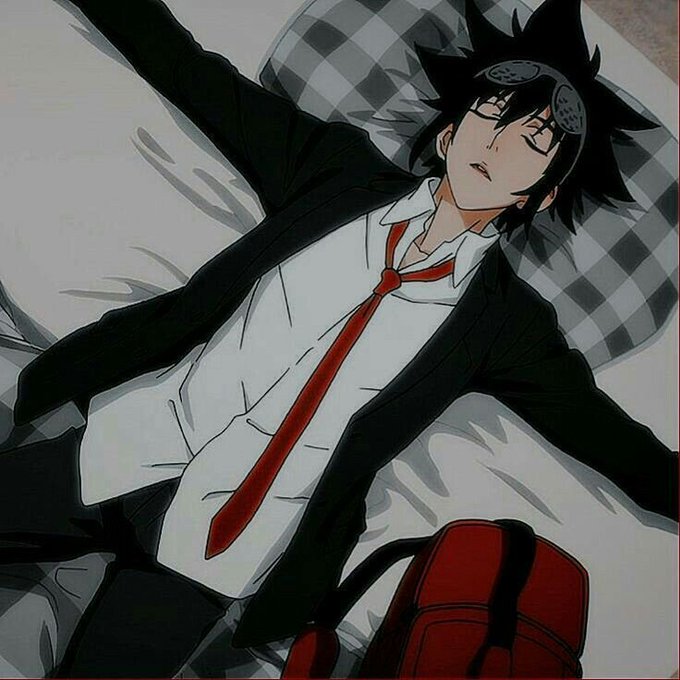 An anime-style illustration of a young man with spiky black hair lying on a bed with checkered pillows, wearing a black suit, white shirt, and red tie, with a red backpack nearby.