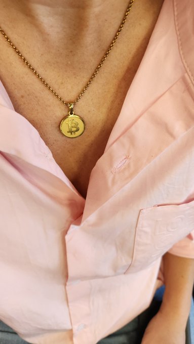 A close-up shot of a person wearing an unbuttoned pink shirt and a gold necklace featuring a Bitcoin pendant.