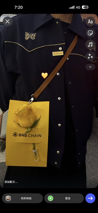 A Snapchat-style photo of someone wearing a dark shirt with a butterfly design, carrying a yellow BNB Chain branded bag with a rose decoration.