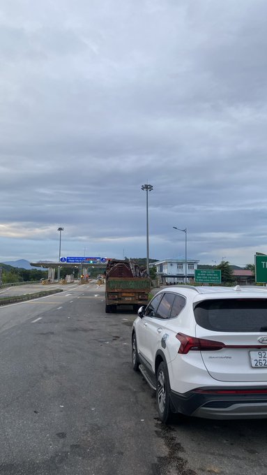 A view from a vehicle approaching a toll plaza under an overcast sky, with a white Hyundai Santa Fe SUV in the foreground and a small truck ahead on the highway.
