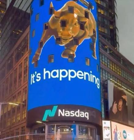 The Nasdaq digital display in New York City features a blue lion graphic breaking through with the text 'It's happening,' below the Nasdaq logo.