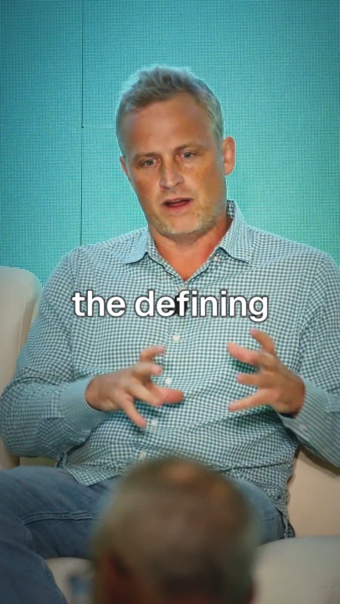 A man in a blue checkered shirt speaking and gesturing with his hands, with the text 'the defining' overlaid on the image.