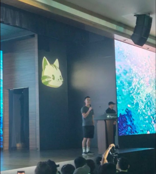 A presenter on stage at what appears to be a Hyperliquid event speaks into a microphone, with the platform's signature cat logo displayed prominently on a large screen beside him. The "purr" caption aptly captures both the cat-themed branding and the playful community spirit of the event.