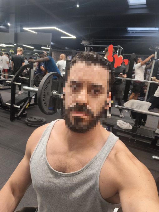 A man with a pixelated face wearing a gray tank top takes a selfie in a gym, with an animated red 'thumbs up' graphic near his head.