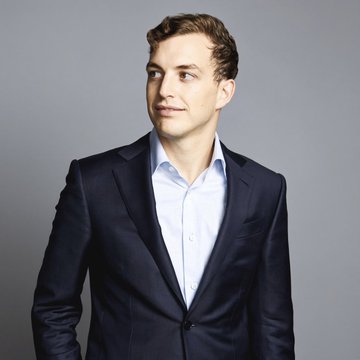 A man in a dark navy suit and light blue dress shirt stands against a gray background, appearing contemplative in a professional headshot. The image likely accompanies an article about World Liberty's Zach Witkoff disputing Justin Sun's claims regarding a court hearing over frozen assets.
