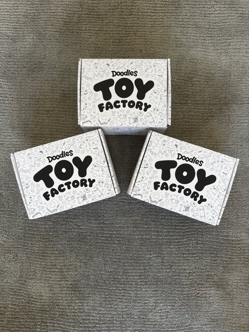 Three white boxes labeled 'Doodles Toy Factory' arranged on a dark gray textured surface.