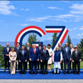 A low-resolution image showing a group of people posing in front of a large "7" logo and outdoor display, likely from a corporate or product event.