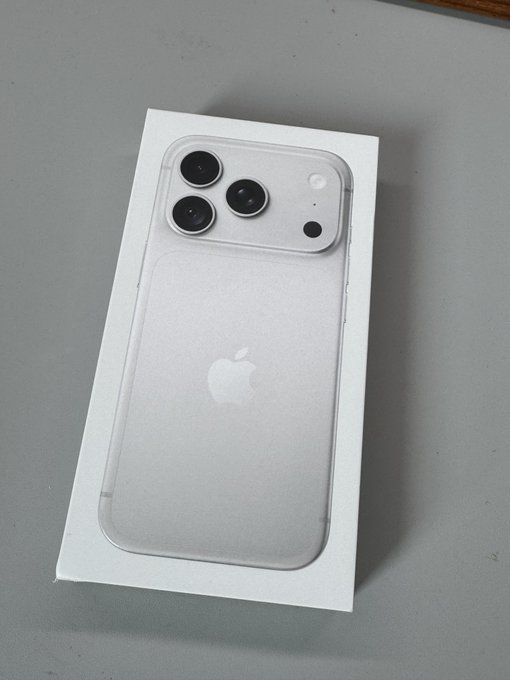 An iPhone with its back cover removed, showing the camera module and Apple logo, resting on a white box on a gray surface.