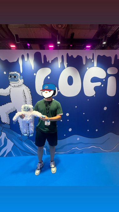 A person wearing a hat and a face mask holds a plush toy while standing in front of a blue "COFi" backdrop at what appears to be a crypto event, fitting the context of the Sui Basecamp 2026 conference attended during Token2049 week in Singapore.