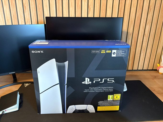 A Sony PlayStation 5 Digital Edition box, 825GB with 4K and HDR support, sits on a desk in front of a monitor.