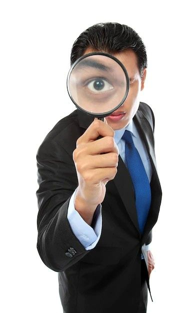 A man in a black suit and blue tie holds a magnifying glass up to his eye, making it appear larger against a white background.