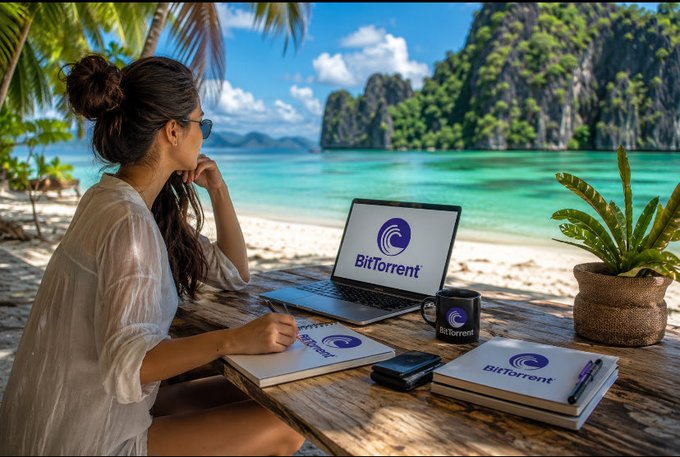 A person works remotely on a tropical beach, with a laptop, notebook, and mug all displaying the BitTorrent logo, reflecting the adaptability of decentralized technology.