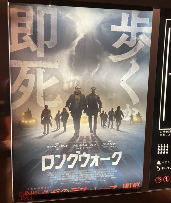A Japanese movie poster for "ロングウォーク" (The Long Walk) displayed in a theater, featuring silhouettes of walking figures against a dramatic backdrop with cast names including スターリング・カリン (Starlight Karin), クーパー・ホフ (Cooper Hoff), and ジュニ・モルケ (Juni Molke) in Japanese text. The poster ties to the post's "#ロングウォーク #STEPN" tags, though the hashtag #STEPN appears unrelated to the actual Stephen King film adaptation being advertised.