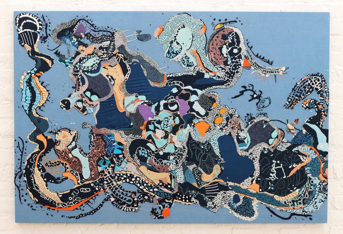 An abstract painting on canvas featuring swirling, intricate patterns in shades of blue, black, white, orange, and purple, mounted on a white brick wall. The artwork's chaotic, psychedelic energy visually matches the caption's exclamation of amazement, as if capturing a sense of awe through its wild, flowing forms.