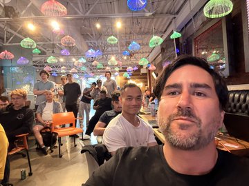 A selfie of two men at a restaurant decorated with colorful jellyfish-shaped hanging lights.