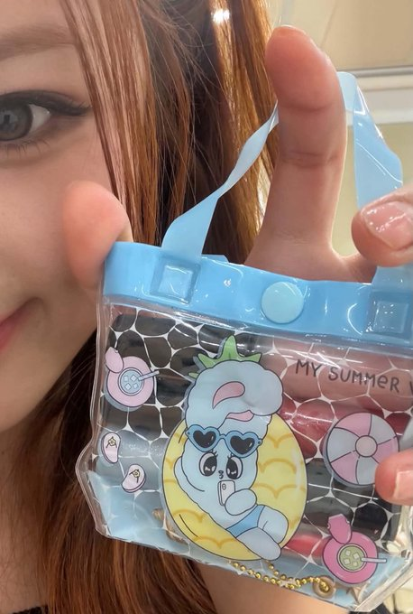 A close-up of a person holding a clear, blue-trimmed small handbag featuring a cartoon character swimming with an inner tube, decorated with buttons, a chain strap, and the text 'MY SUMMER'.