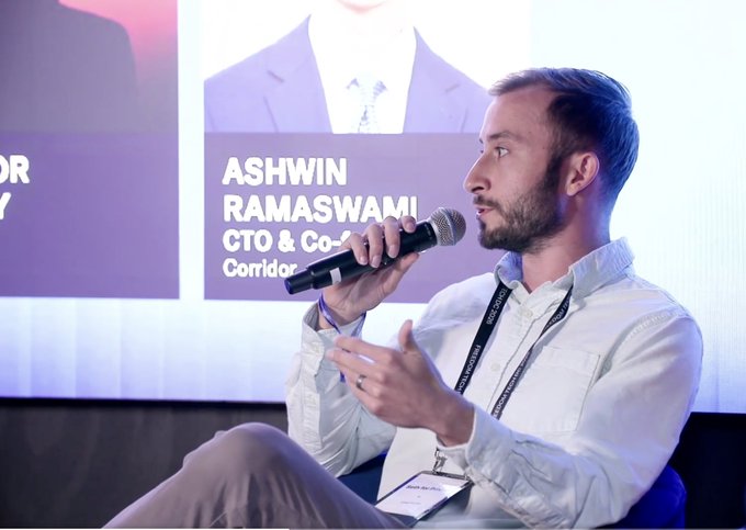 A man with a beard holds a microphone while speaking on a panel, identified by a screen behind him as "ASHWIN RAMASWAMI, CTO & Co-..." representing "Corridor."