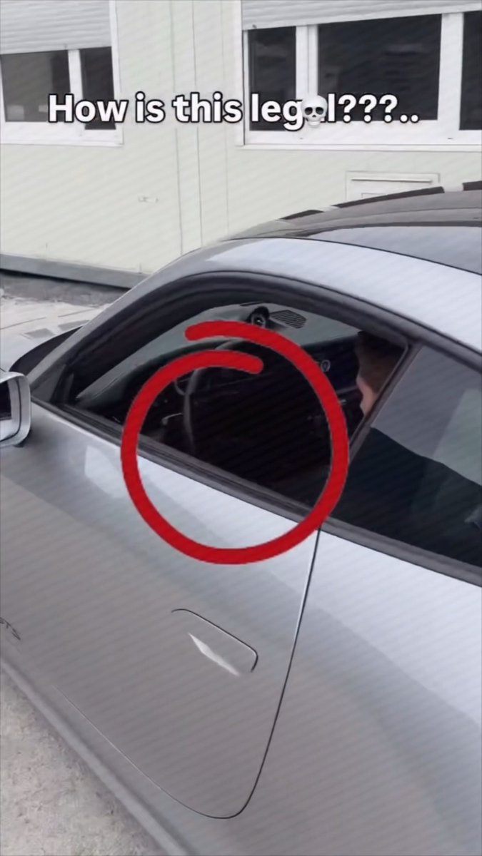A meme photo of a silver car with a red circle highlighting an oddly shaped steering wheel visible through the driver's window, captioned 'How is this legal???' with a skull emoji.