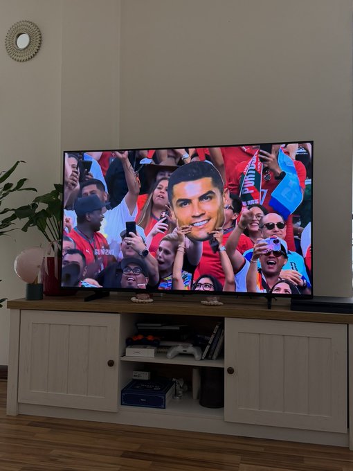 A TV displays a crowd scene featuring a cutout of Cristiano Ronaldo's face, fitting the Saturday Portugal vs. Colombia football match context of the post.