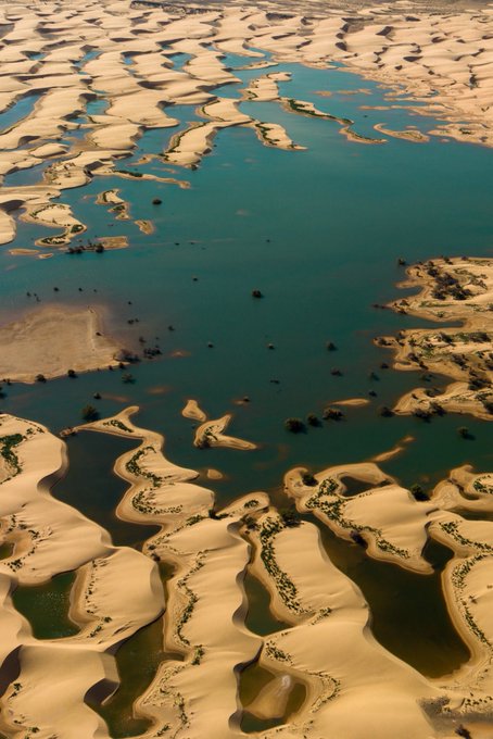 An aerial view of sand dunes interspersed with turquoise water channels, likely depicting Lençóis Maranhenses in Brazil.