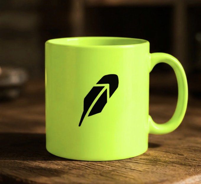 A bright lime-green ceramic mug with a black feather quill logo sits on a wooden surface against a dark background.