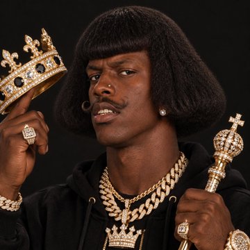 A man with a bowl-cut hairstyle and mustache holding a jeweled crown and a scepter, wearing gold chains and a black hoodie against a black background.