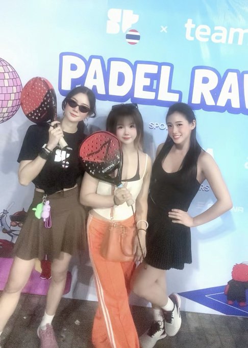 Three women pose with red padel rackets in front of a banner that reads "PADEL RA..." and "team".