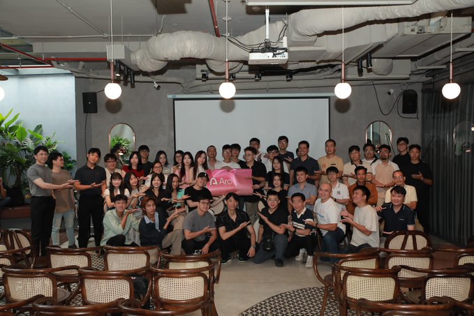 A large group photo of people posing indoors, holding an 'Arc' branded sign.