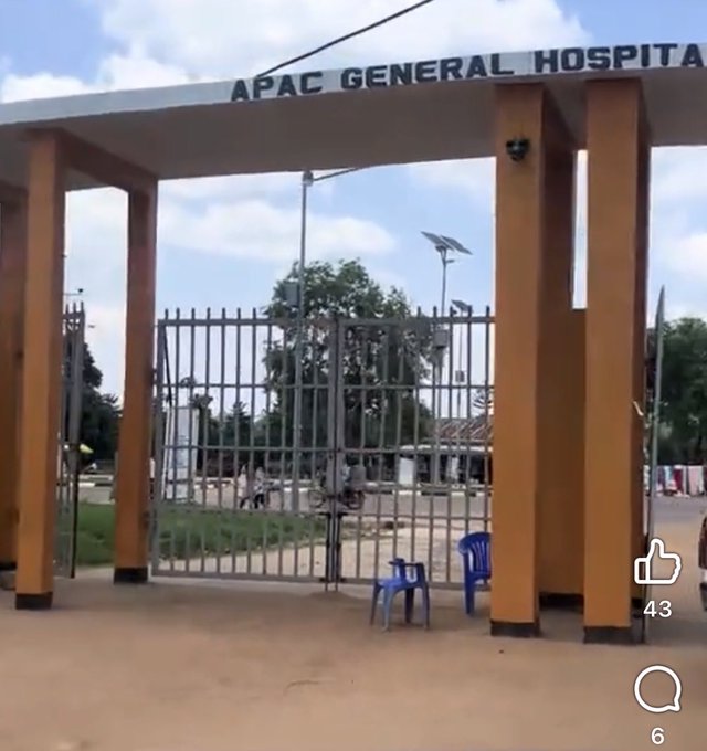 The entrance to Apac General Hospital features a large metal gate flanked by tall orange pillars, with a small blue plastic chair sitting just inside the gate. The caption "75M gate" likely refers to the UGX 75 million cost reportedly spent on constructing this hospital gate in Uganda.