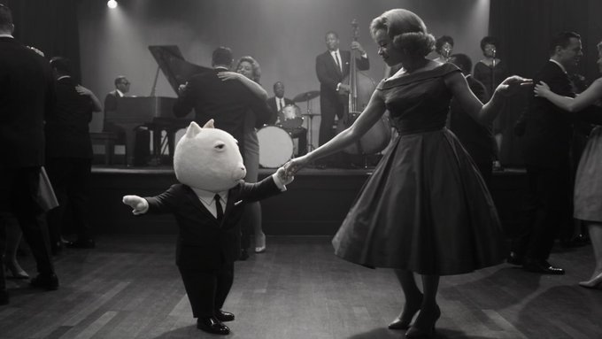 A surreal black and white image showing an anthropomorphic white bear in a suit dancing with a woman in a vintage dress at a 1950s-style ballroom with a live band.